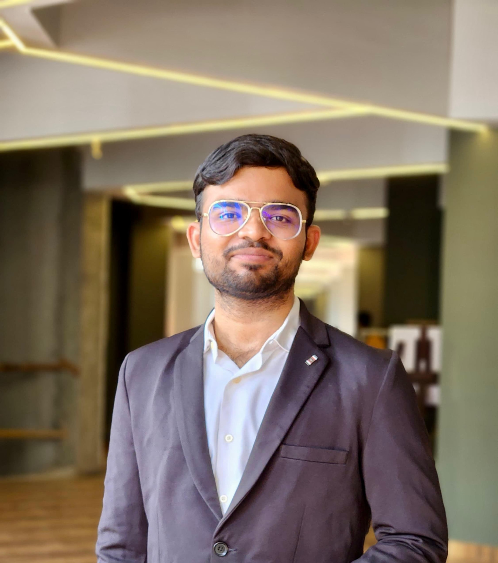 Portrait of Shaik Simalullah, founder and architect of IMARAH, wearing a dark blazer in a softly lit architectural corridor